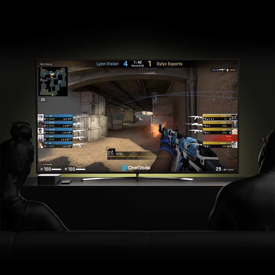 A live Twitch stream of OneQode’s Guam Gaming Tournament playing on a television, with two people sitting on a couch watching